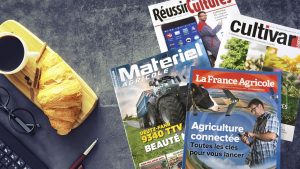 Rechts auf dem Bild sind vier Zeitschriften der Ausgaben La France Agricole, Matériel Agrocile, Cultivar und Réussir Grandes Cultures zu sehen. Links auf dem Bild liegt ein Holzbrett mit einer Kaffeetasse und einem Croissant drauf. Links unten in der Ecke sieht man den Anschnitt einer Computertastatur und eines Stifts.